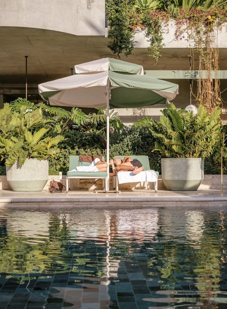Huéspedes relajados junto a la piscina, tumbados bajo una sombrilla en un patio soleado