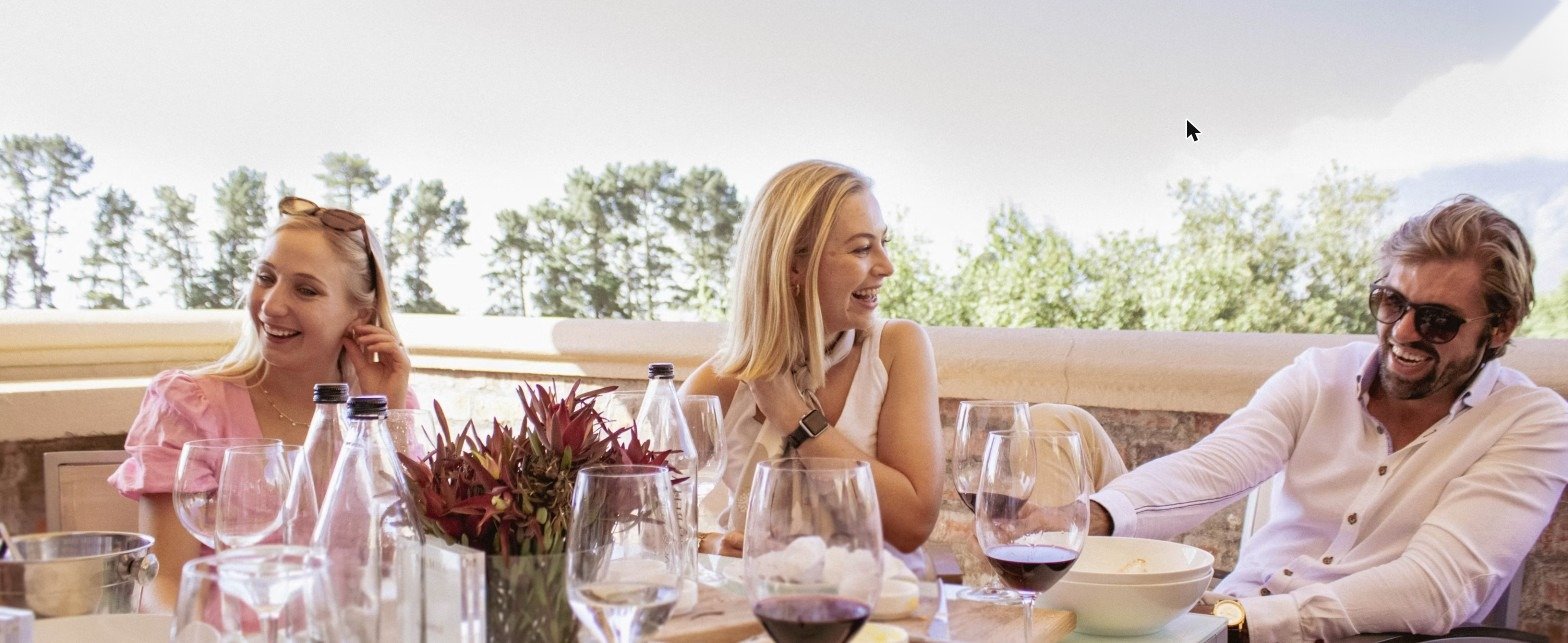 Huéspedes almorzando en una terraza elegante del hotel, copas de vino sobre la mesa, luz de mediodía