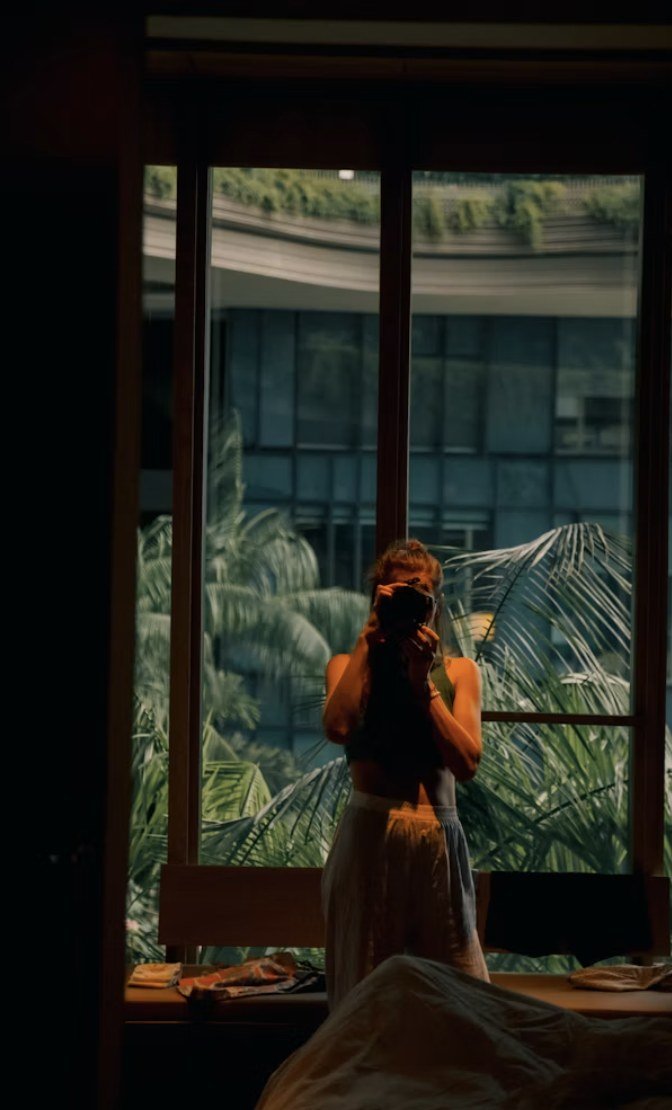 Fotógrafa a contraluz haciendo una fotografía junto a una ventana con vegetación de fondo