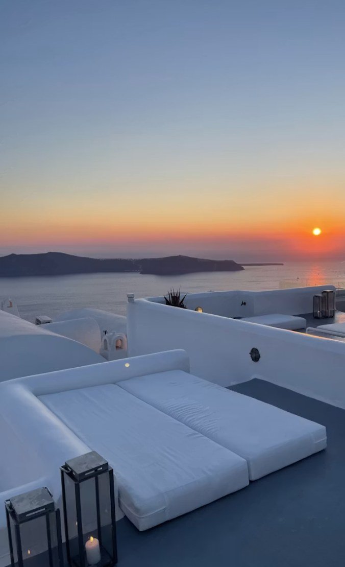 Tumbonas blancas en una azotea con vistas al mar durante la puesta de sol
